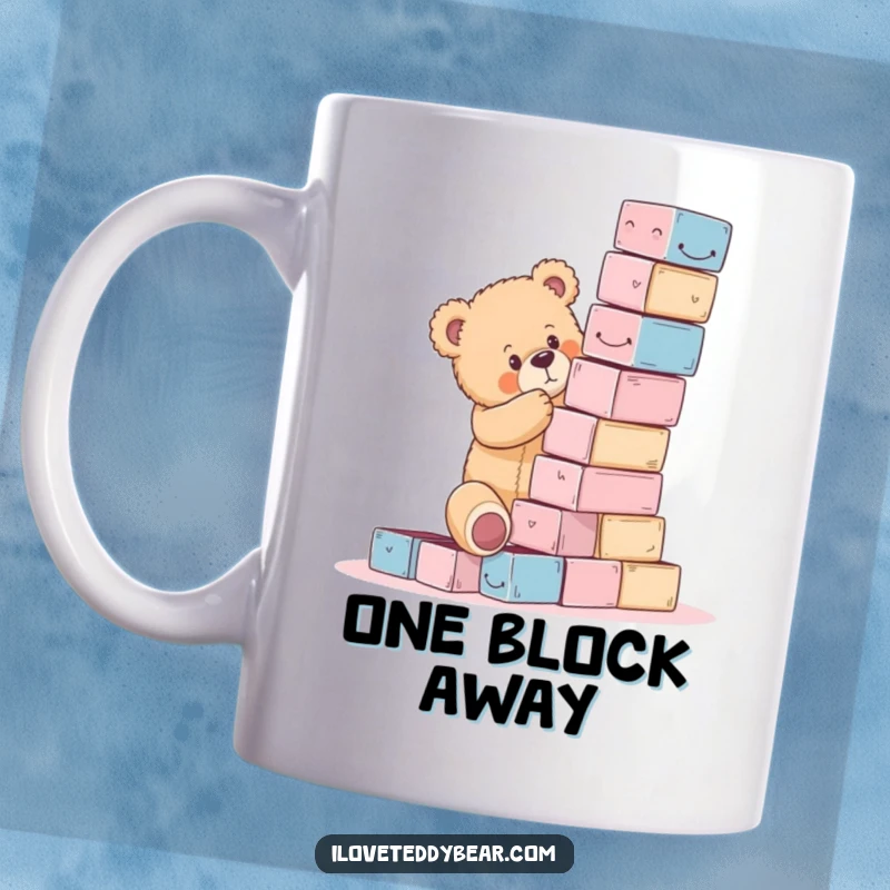 Funny teddy bear mug showing a bear struggling to build a wobbly tower of blocks that’s about to tumble.