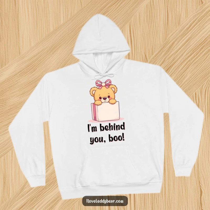 Funny hoodie with a teddy bear peeking playfully from behind a large, shimmering present, embodying warmth and surprise.
